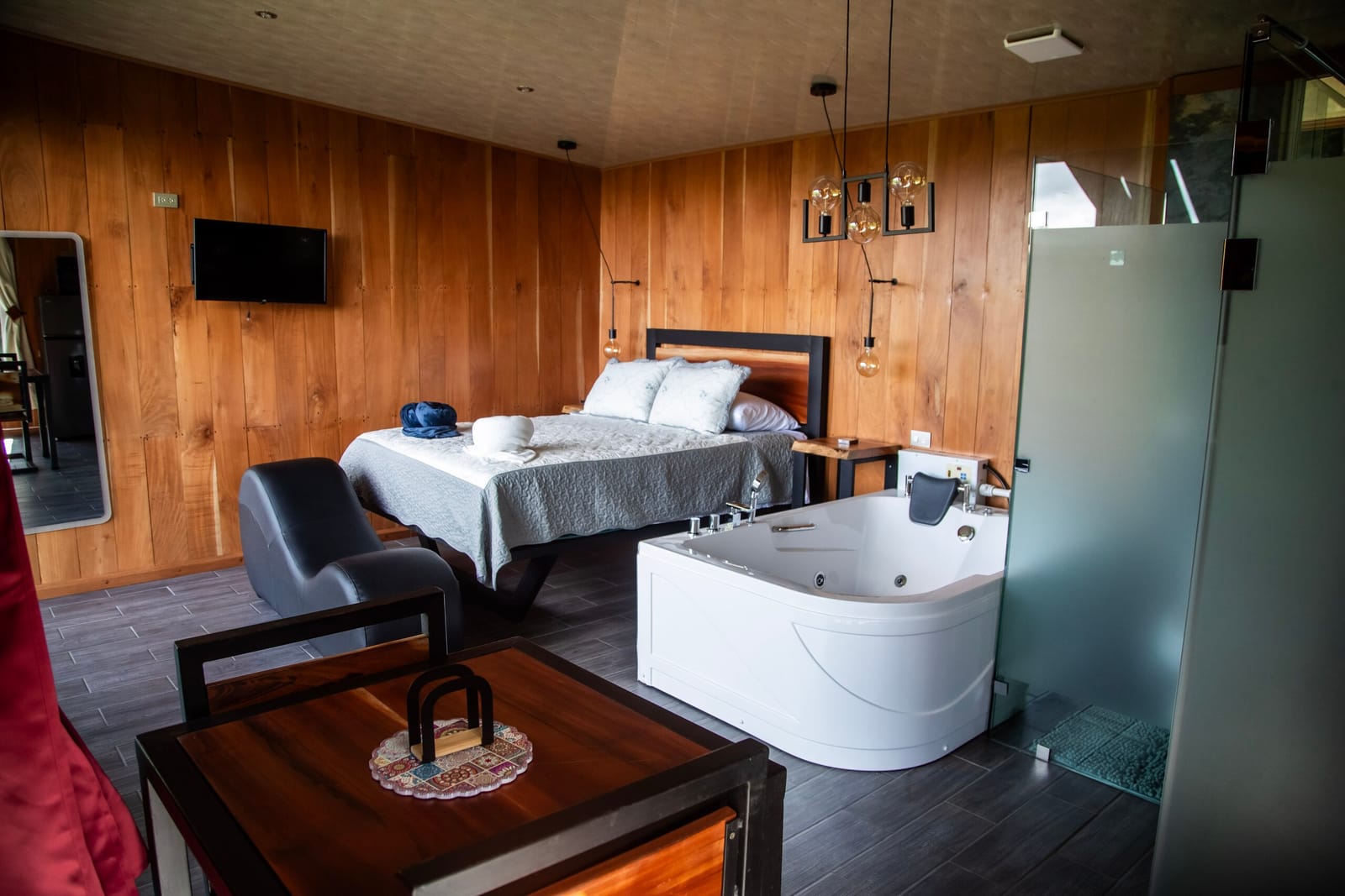 Wood-clad room with queen bed, jacuzzi and dining table