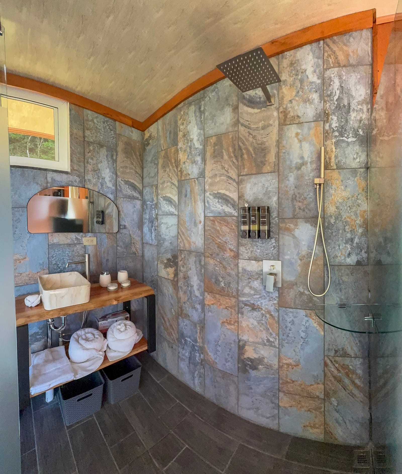 Stone-tiled shower with rain head and wood vanity