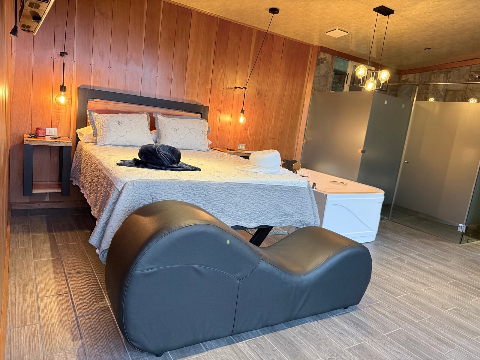 Queen bed under pendant lights with wood-clad walls