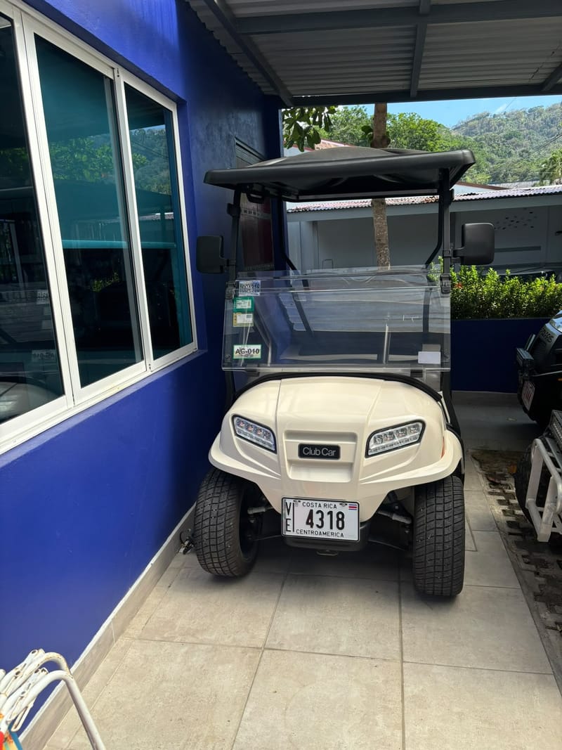 White Club Car golf cart in the carport beside the blue wall