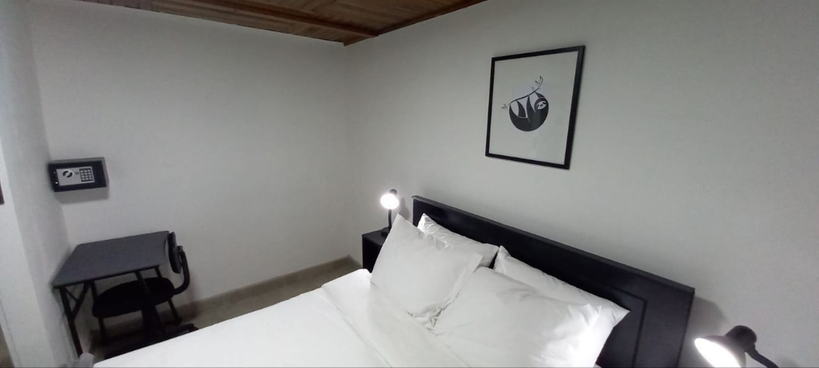Bedroom with dark headboard, reading lamps and a sloth print