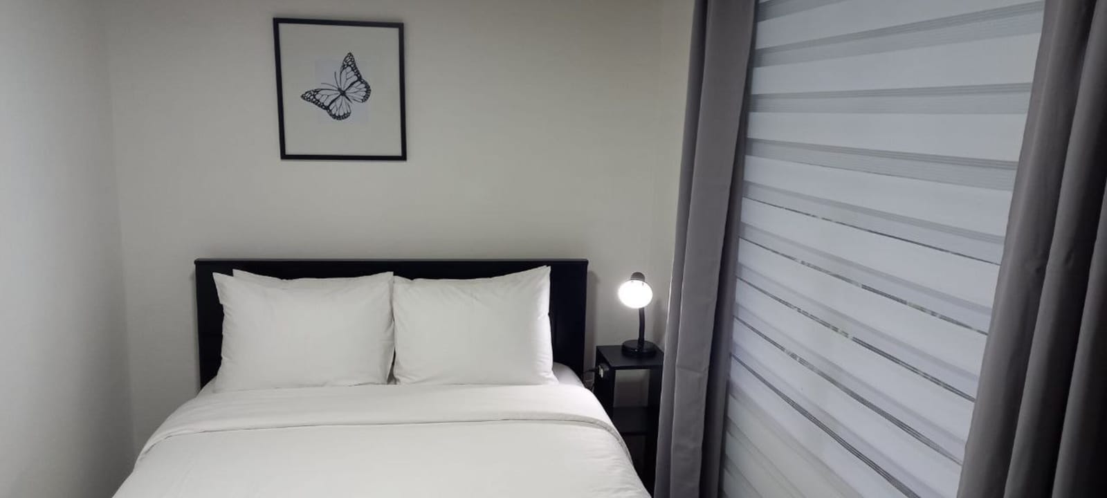 Bed with white linens beside a striped roller blind