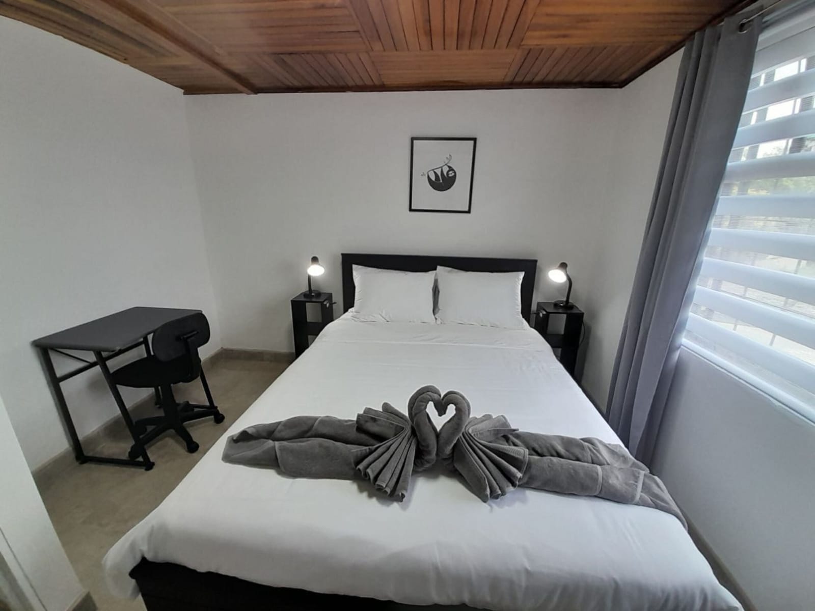 Queen bed with folded towels and a desk in the corner
