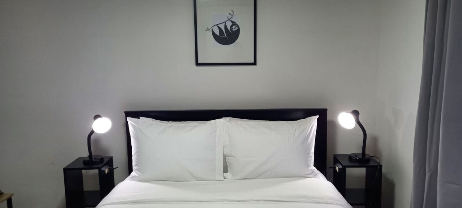 Bed with white pillows under a framed sloth print