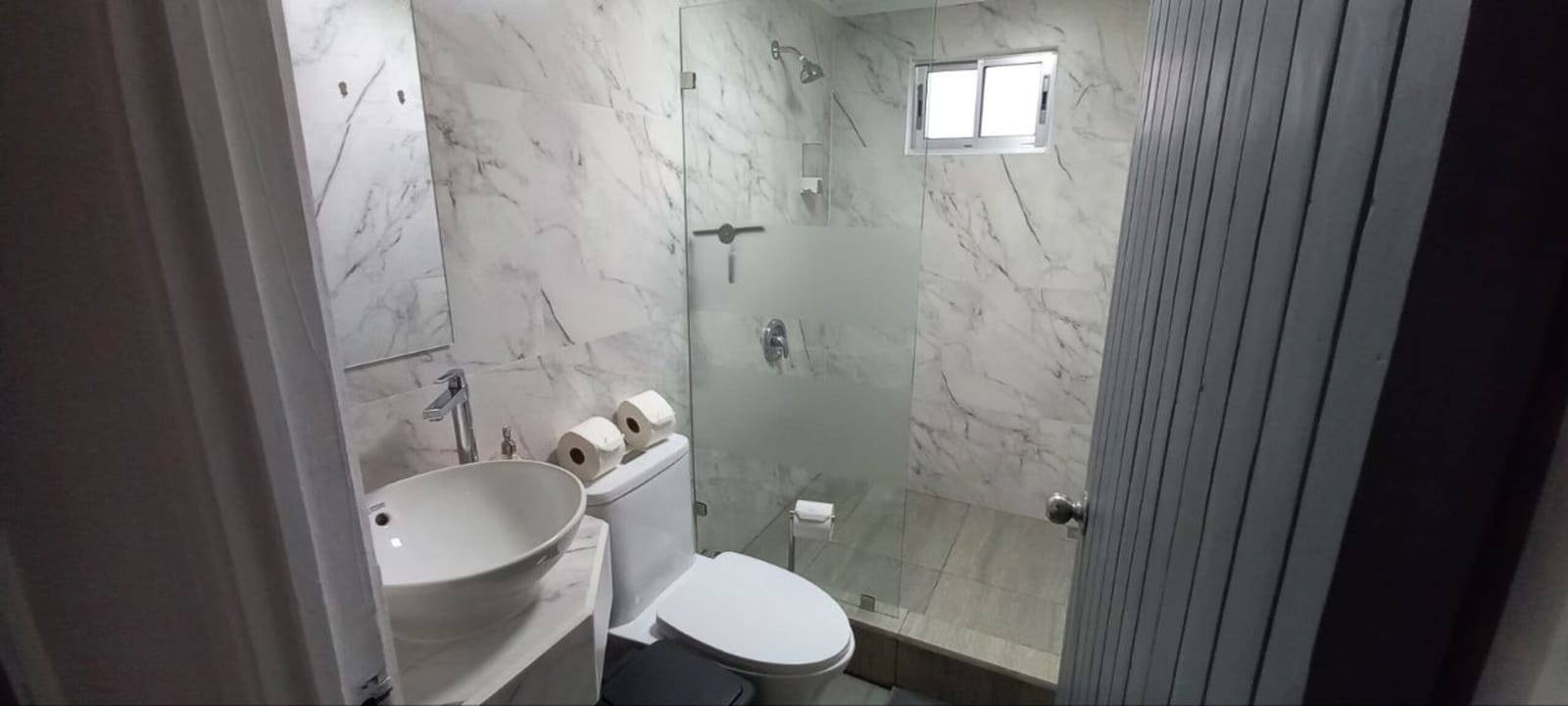 Bathroom with marble tiles, glass shower and small window