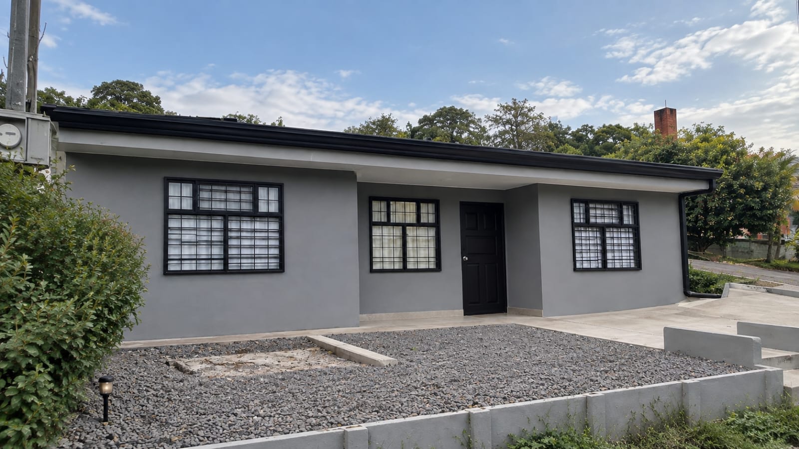 Gray single-story house with black window frames and a gravel front yard in Santa Elena