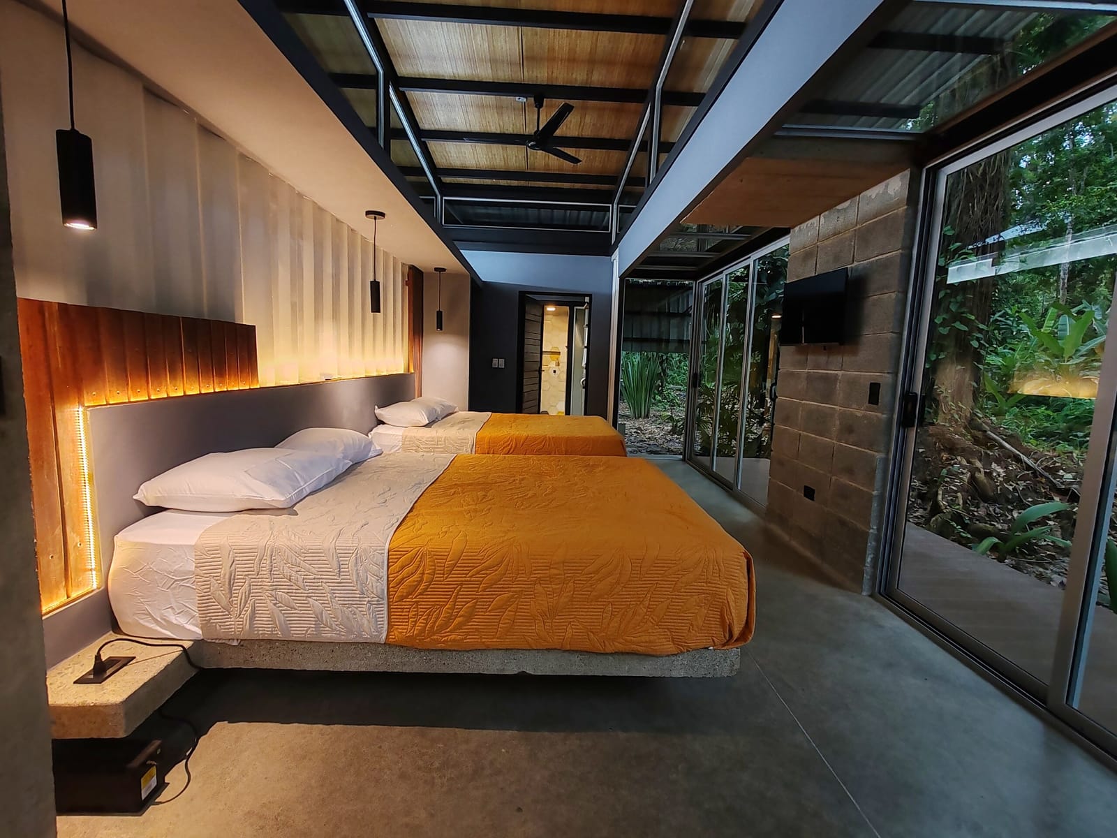 Queen beds with orange and white covers under pendant lights