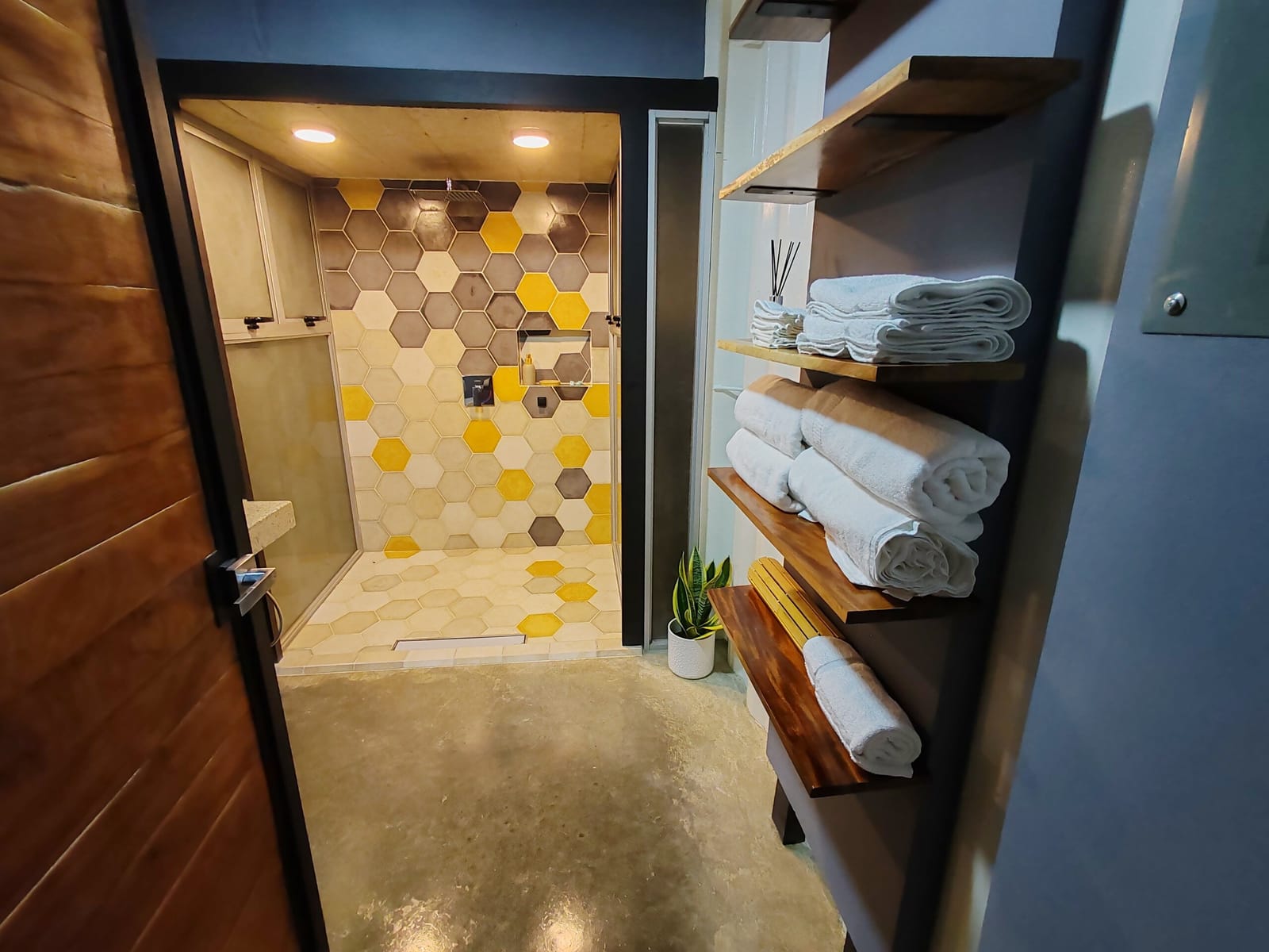 Hexagon-tiled shower with wooden towel shelves beside it