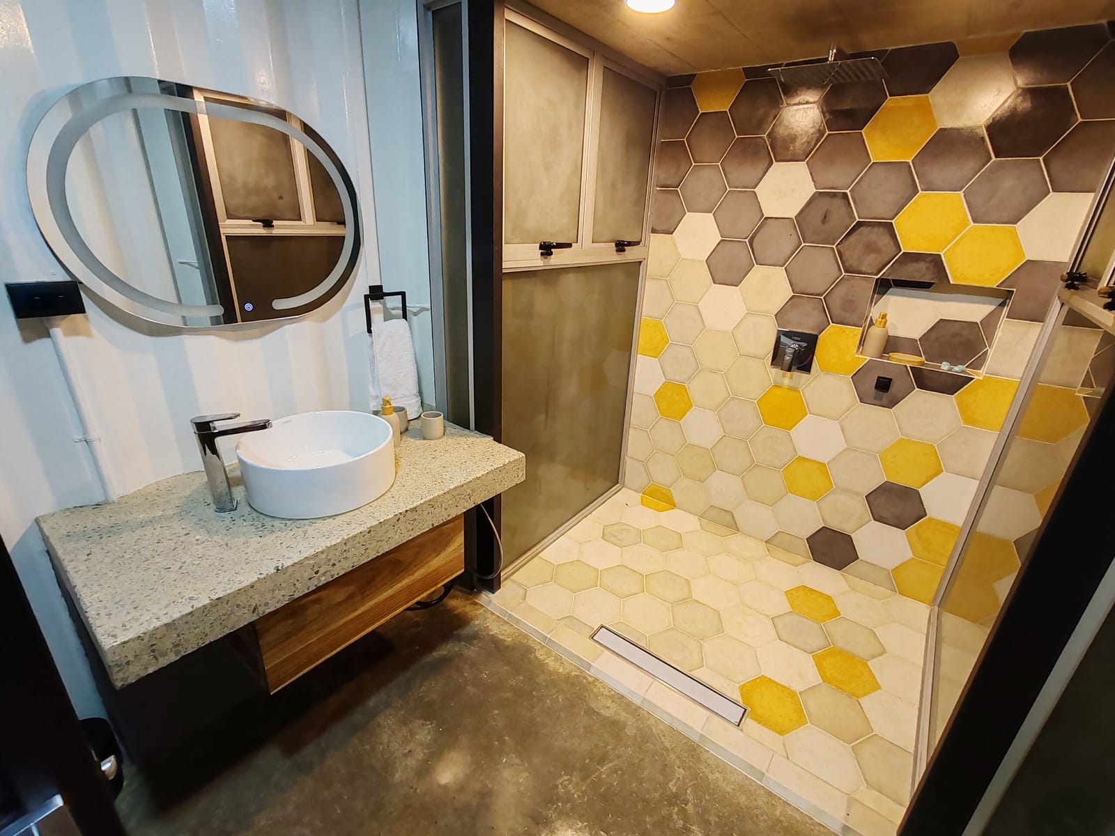 Hexagon-tiled walk-in shower with round mirror and vessel sink