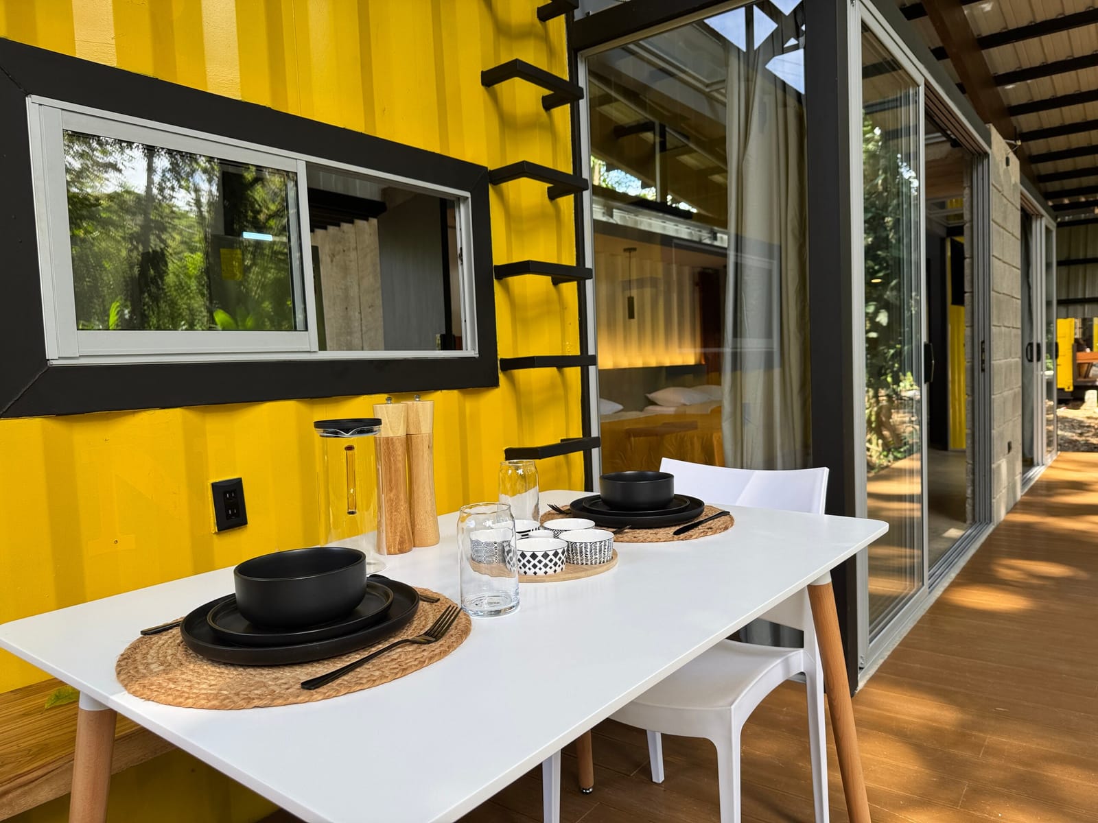 White dining table on the deck beside the yellow wall