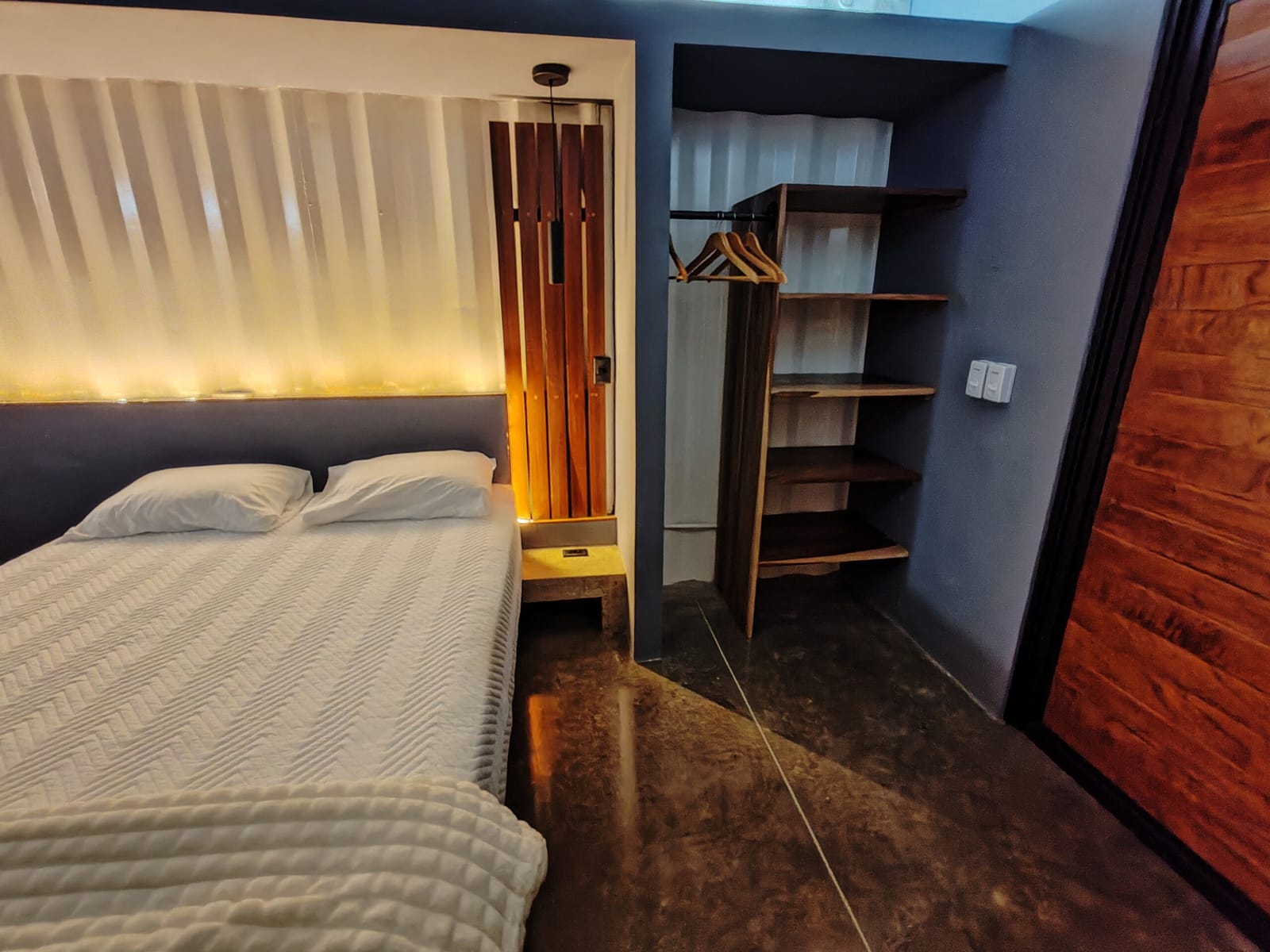 Bed with lit headboard beside an open wooden wardrobe