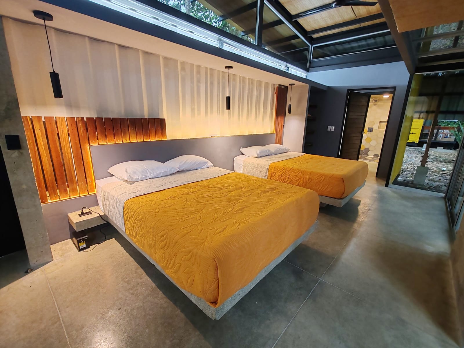 Two queen beds with orange covers facing the glass wall