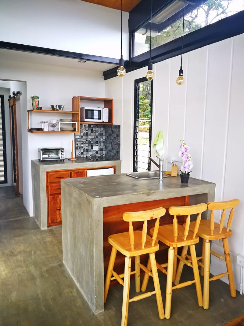 Concrete kitchen island with three wooden stools and pendant lights