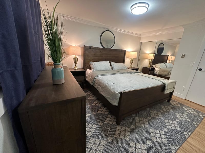 King bed with dark wood frame, dresser and round mirror