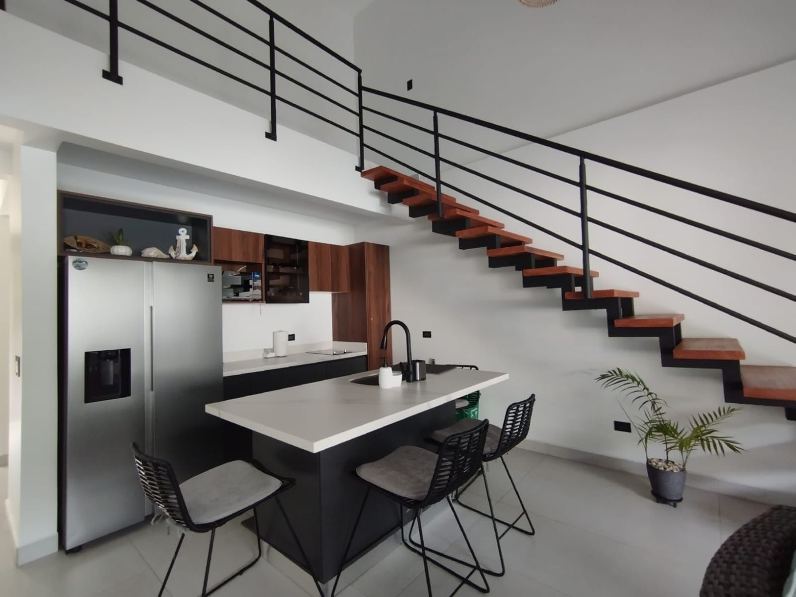 Black kitchen island with stools beneath the floating stair
