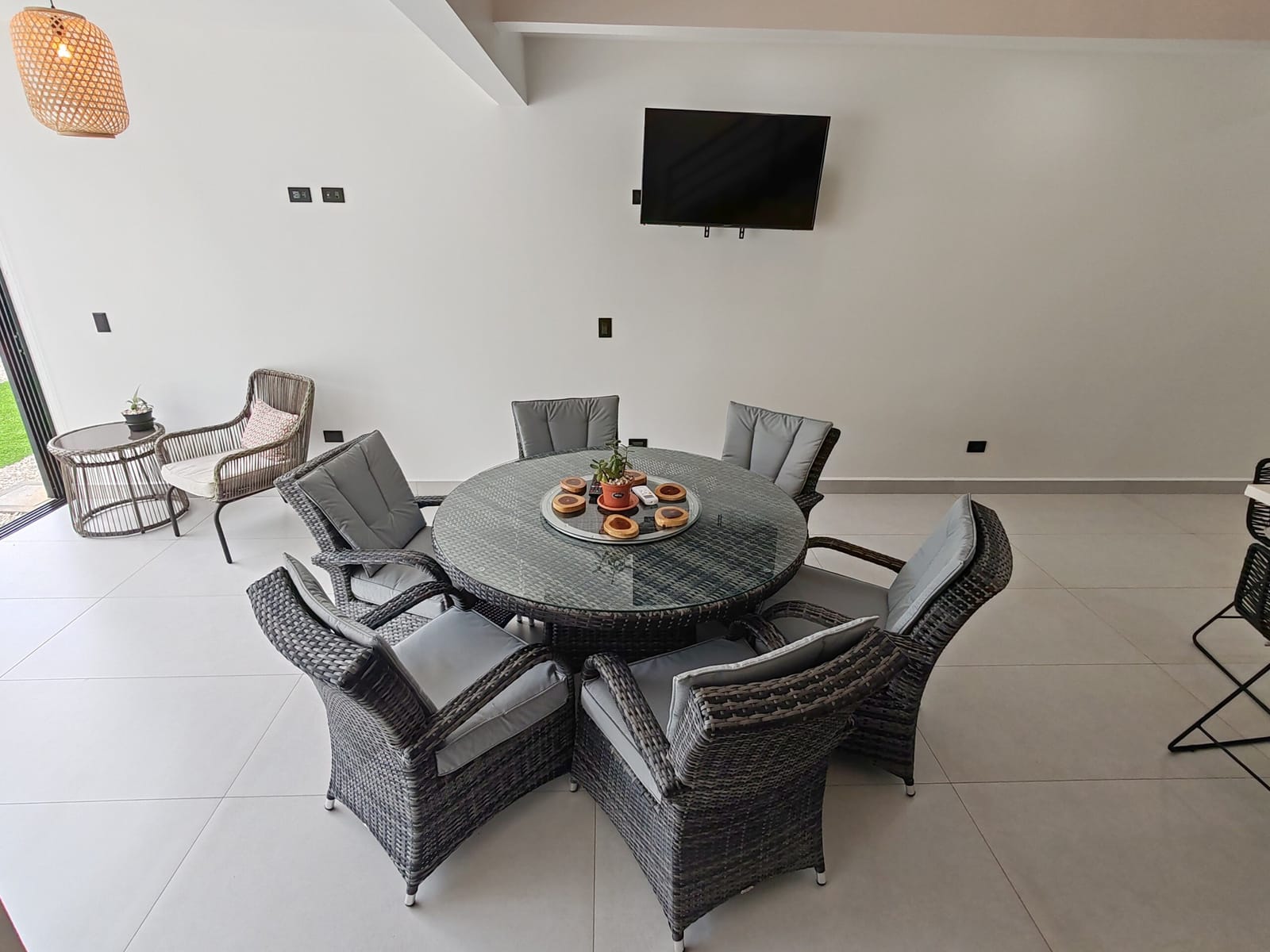Round table with gray rattan chairs and wall TV