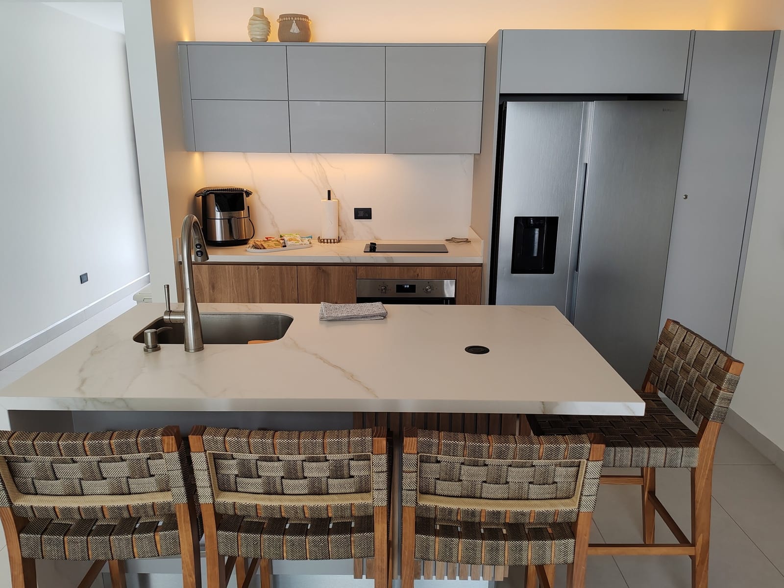 Marble-look island with sink, woven stools and stainless refrigerator