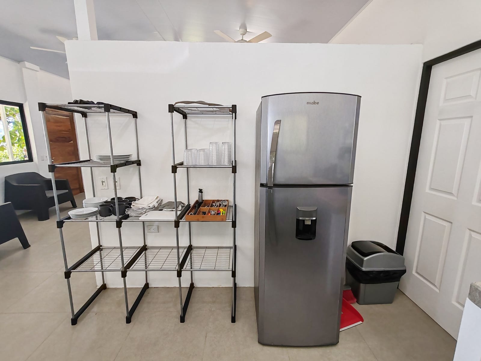 Metal kitchen shelves with dishes beside the gray refrigerator